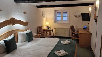A bedroom with a wooden bed, a desk, a chair, a lamp, a TV, and a window.
