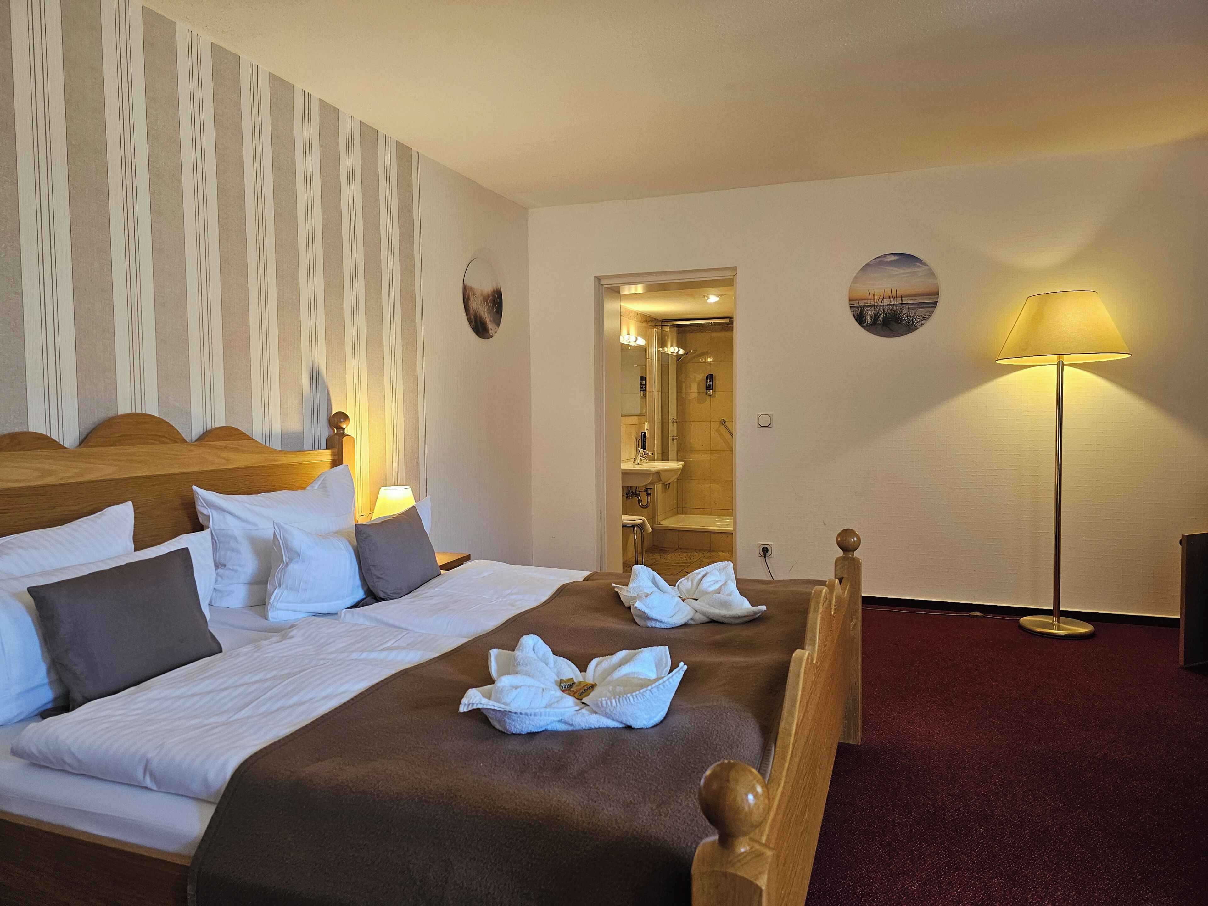 Una habitación de hotel con cama, mesita de noche, lámpara y zona de ducha.