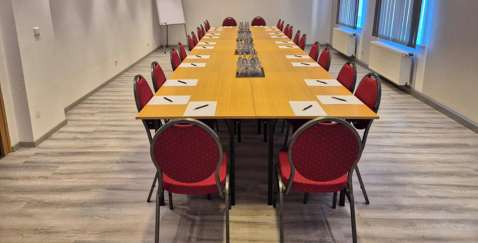Un salón de conferencias con una larga mesa, sillas rojas y una pizarra.