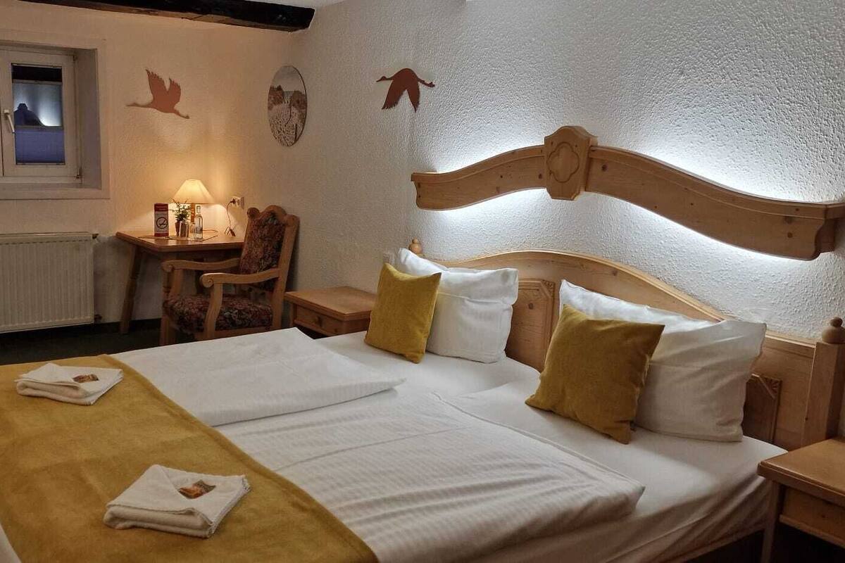 A hotel room with a bed, bedside tables, a desk, a chair, a lamp, and a window.