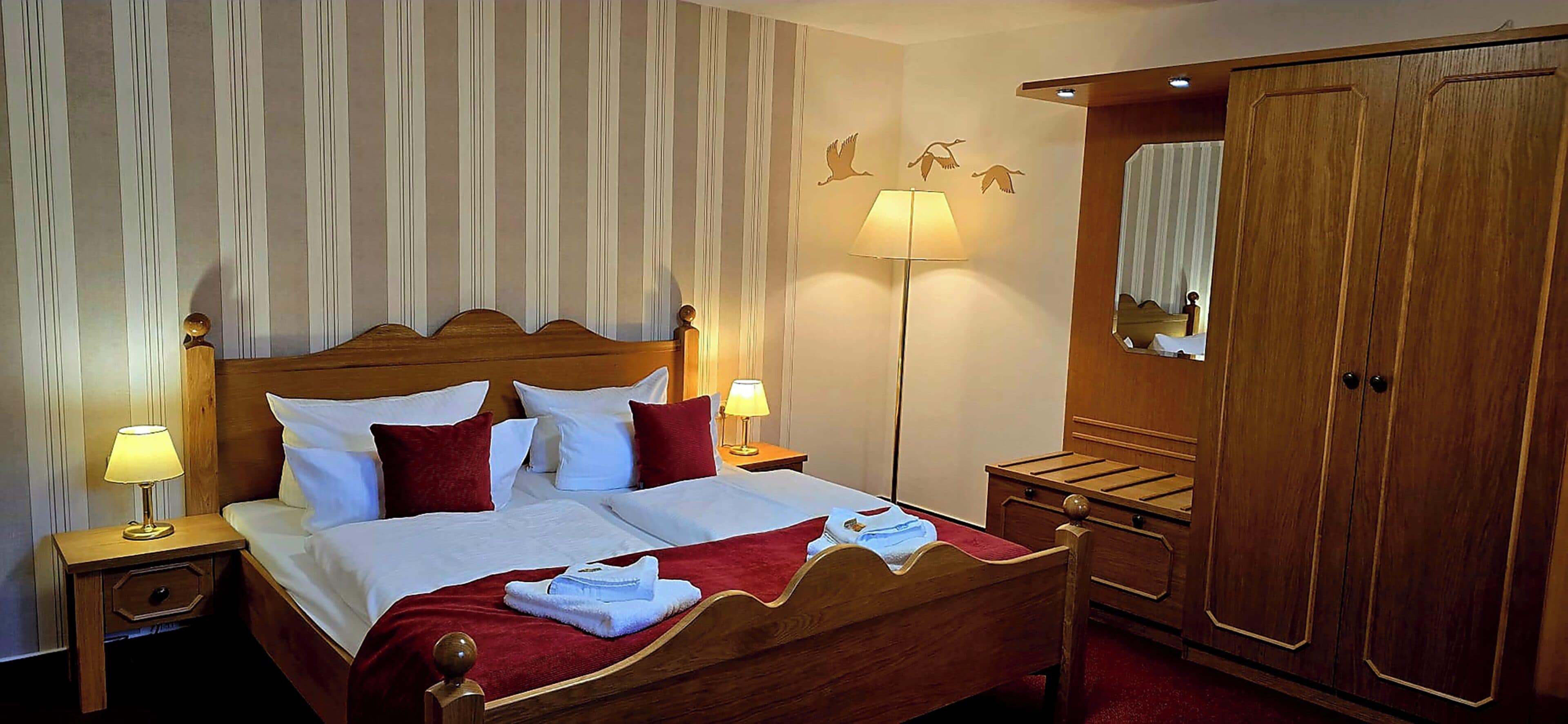 A hotel room with a wooden bed, two bedside tables, a nightstand, a wardrobe, and a mirror.
