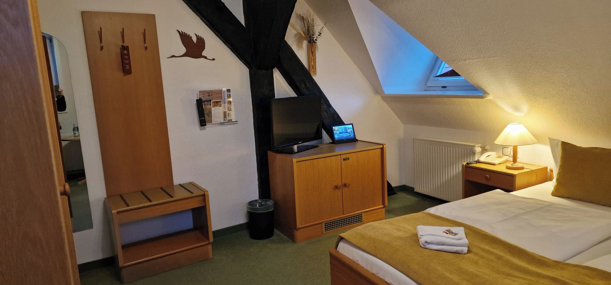 A hotel room with a bed, a desk with a computer, a TV, a lamp, and a window with a view.