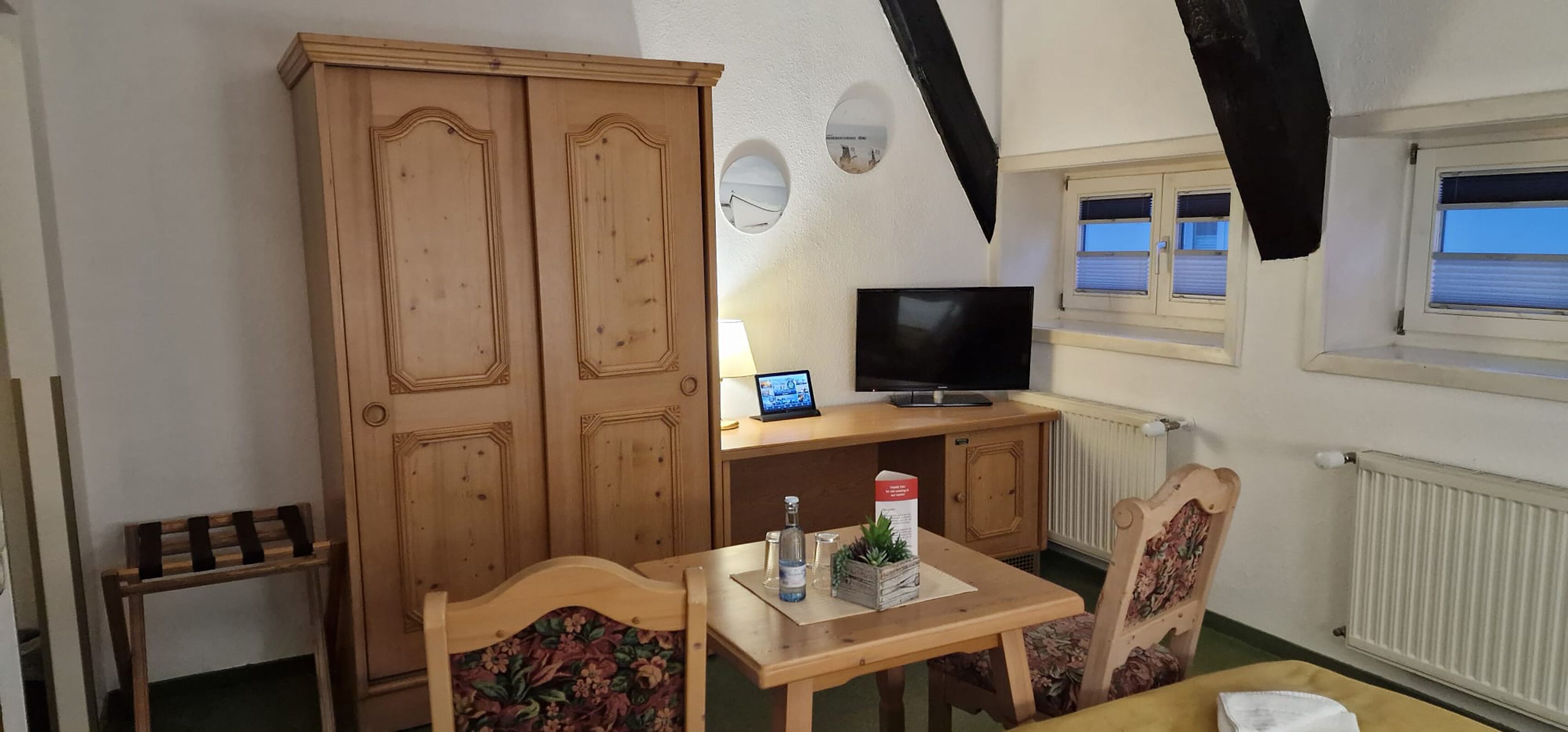 Quarto com guarda-roupa de madeira, televisão sobre uma mesa de madeira e janela com persianas.