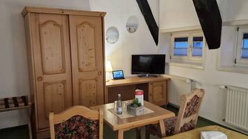 Quarto com guarda-roupa de madeira, televisão sobre uma mesa de madeira e janela com persianas.