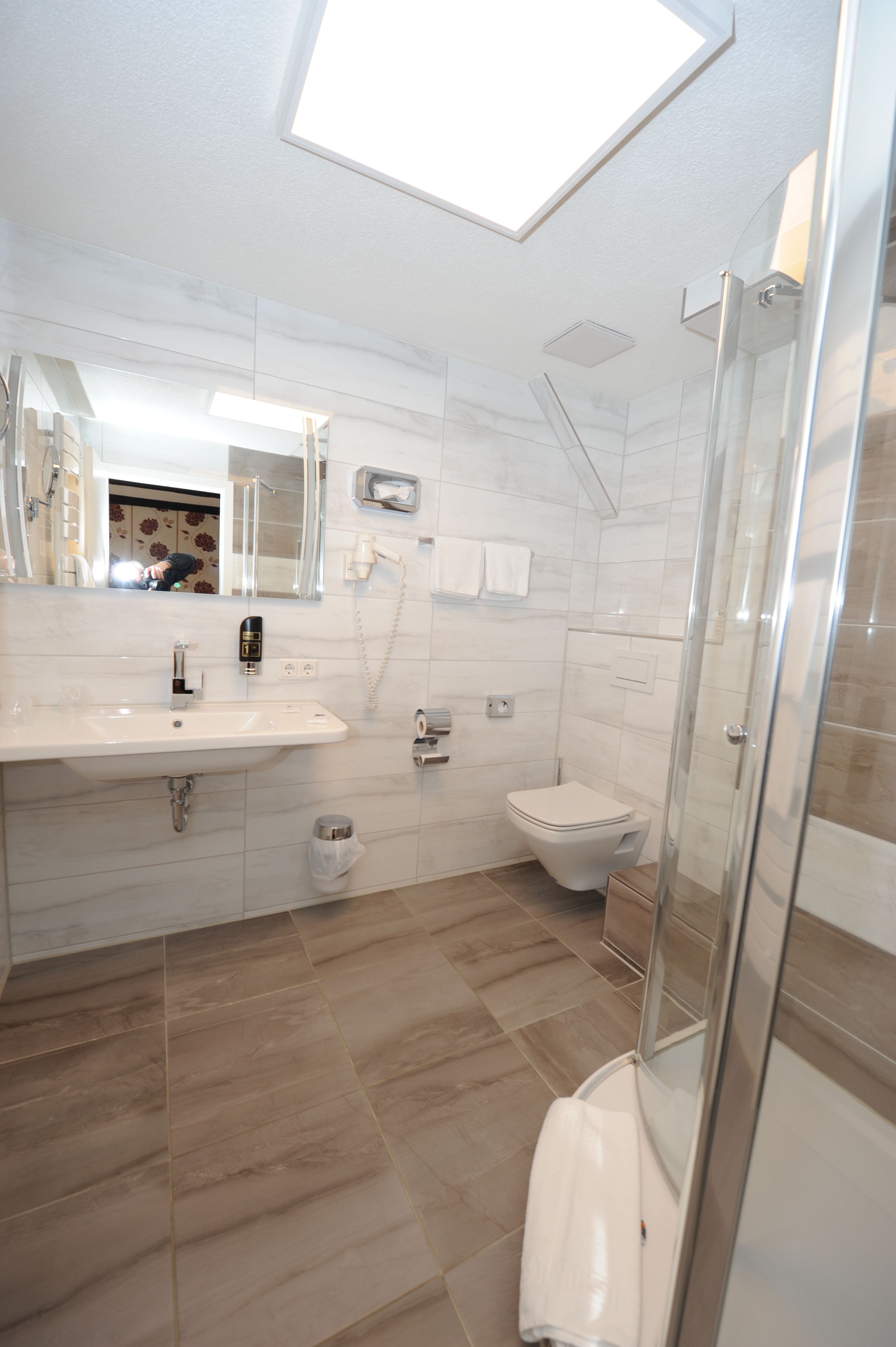 Un baño moderno con tragaluz, un lavabo, un inodoro y ducha con mampara de vidrio.