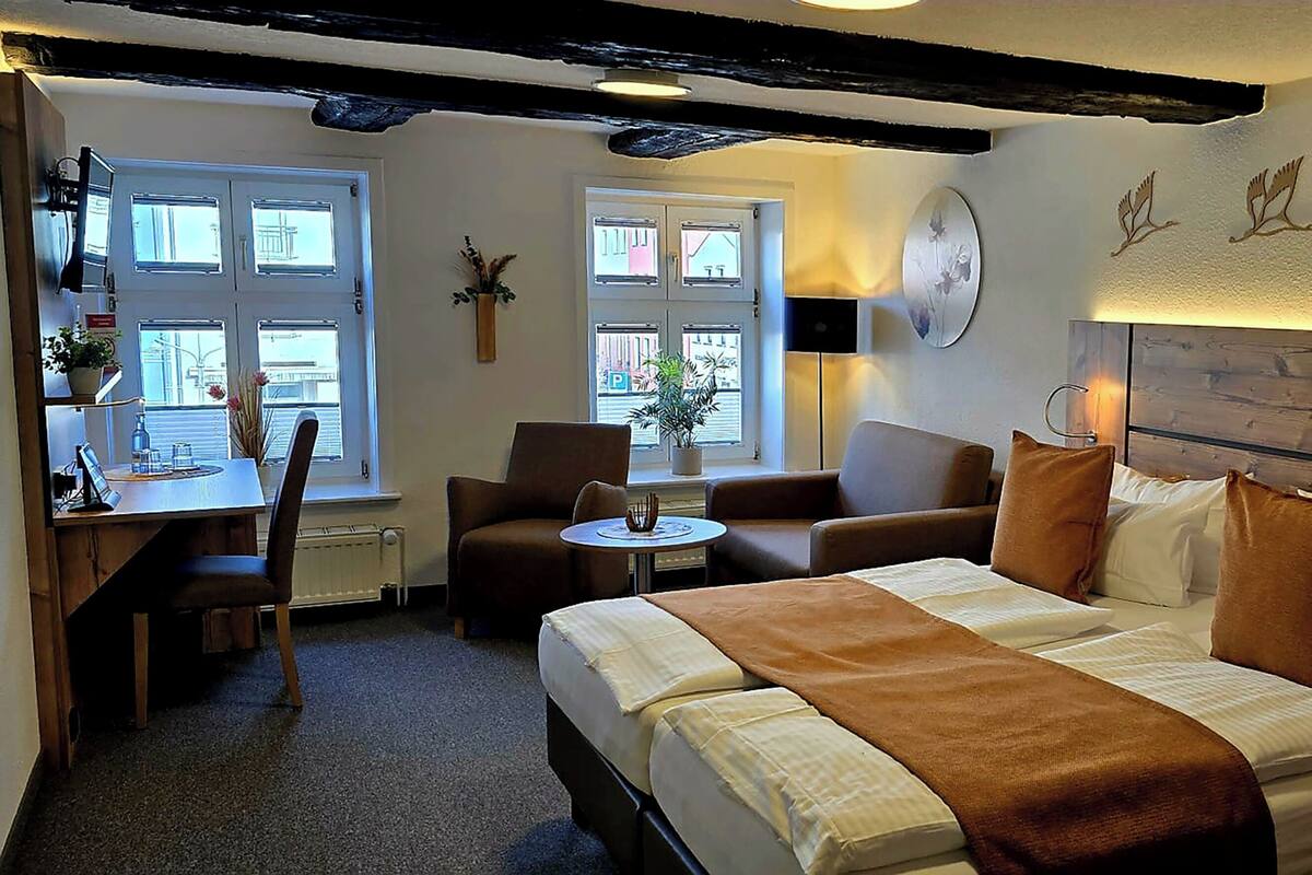 A hotel room with a bed, a desk, a chair, a small table, and a window.