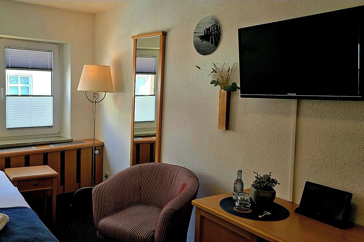 A hotel room with a bed, a desk, a chair, a TV, and a window with blinds.