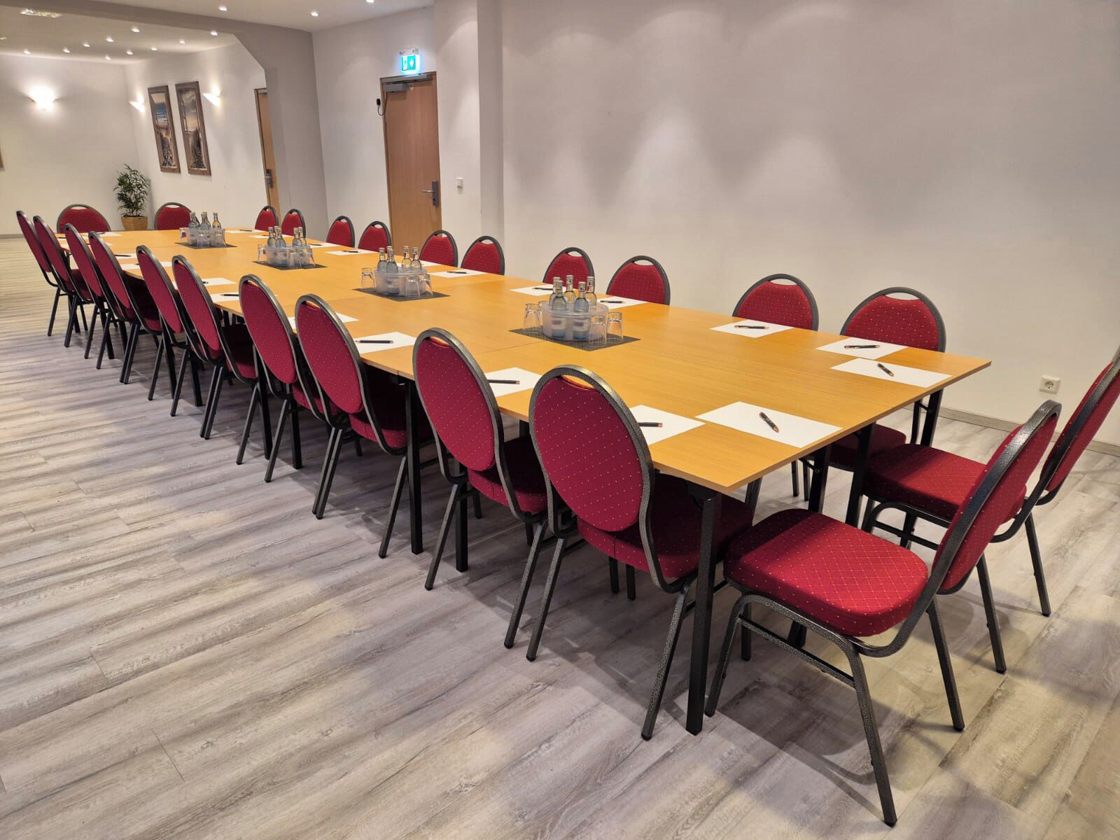 A conference room with a long table, red chairs, and a wooden floor.