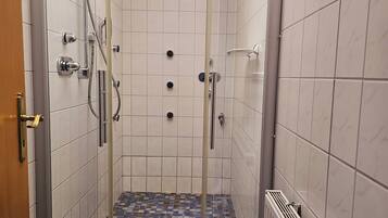 Un espace douche doté d’une porte en verre, de murs recouverts de carreaux blancs et d’un sol à motifs.
