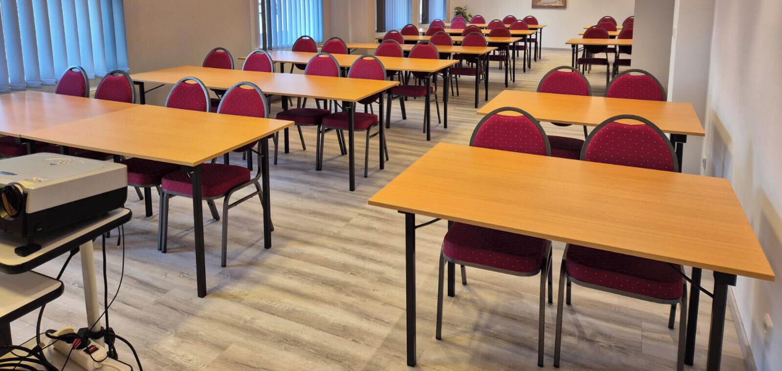 A conference room with multiple tables and chairs, a projector, and a window with blinds.