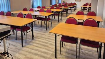 A conference room with multiple tables and chairs, a projector, and a window with blinds.