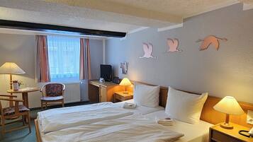 A hotel room with a bed, bedside table, lamp, chair, desk, and a window with curtains.