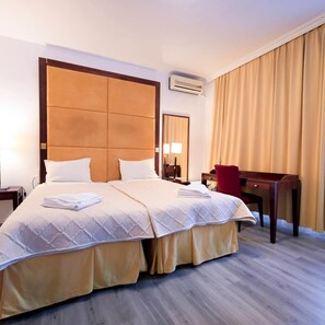 A hotel room with a large bed, a desk, a chair, a lamp, and an air conditioning unit. - Visconti Residence (Bucharest)