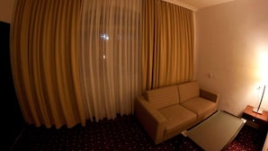 A hotel room with a curved window, a sofa, a small table, and a lamp. - Visconti Residence (Bucharest)