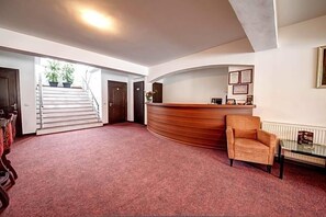 A reception area with a curved desk, a chair, a staircase, and a door. - Visconti Residence (Bucharest)