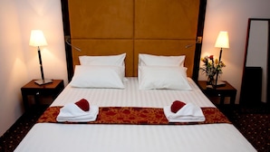 A hotel room with a large bed, two bedside tables with lamps, a vase with flowers, and a mirror on the wall. - Visconti Residence (Bucharest)