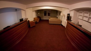 A hotel lobby with a curved wooden reception desk, a beige sofa, and a television on a stand. - Visconti Residence (Bucharest)