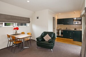 Un espacio habitable compacto con comedor, una butaca de cuero verde, cocina con armarios oscuros y una ventana con vistas.