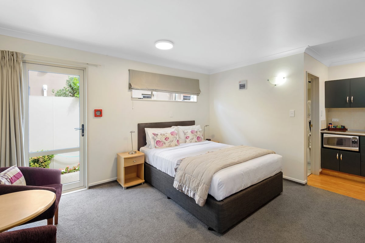 A bedroom with a bed, bedside table, chair, and a view of the outside.