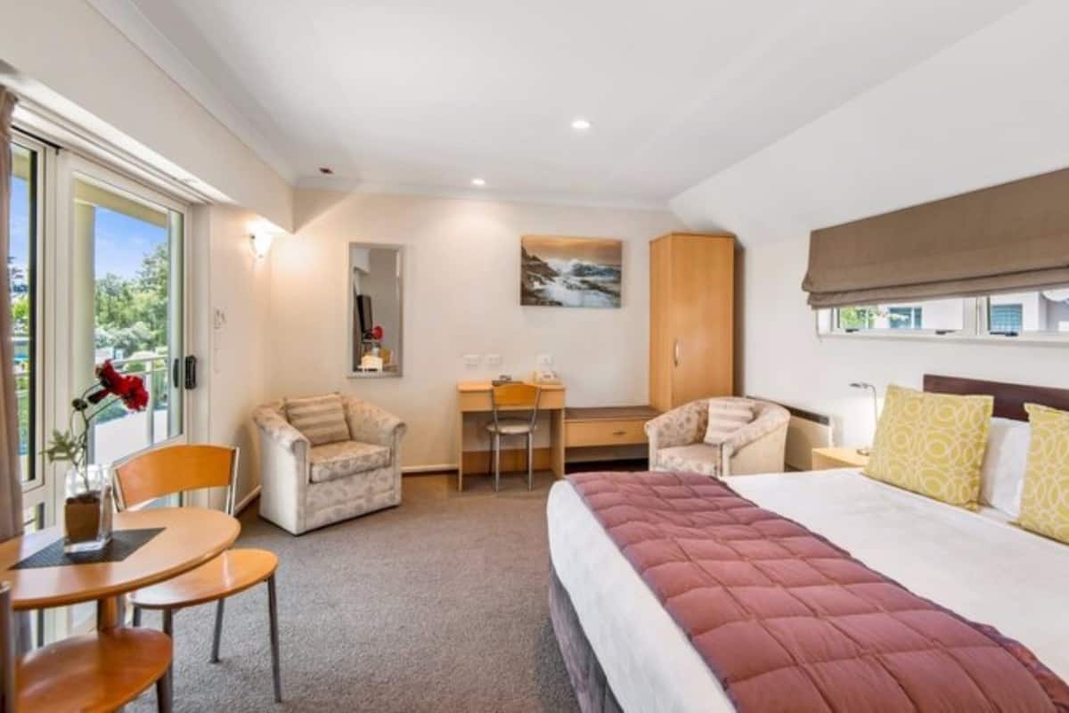 A hotel room with a bed, two armchairs, a desk, and a view of the outdoors.