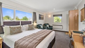 A hotel room with a large bed, two chairs, a desk, and a window with a view of trees.