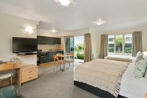 A modern bedroom with a large bed, a desk, and a kitchenette. - Colombo in the City (Christchurch)