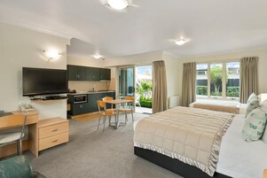A modern bedroom with a large bed, a desk, and a kitchenette.