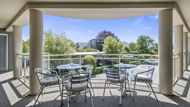 A covered outdoor seating area with tables and chairs, overlooking a parking lot and buildings.