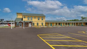 A motel with a large parking lot and a row of rooms with green doors. - Cardinal Motel (Bowling Green)