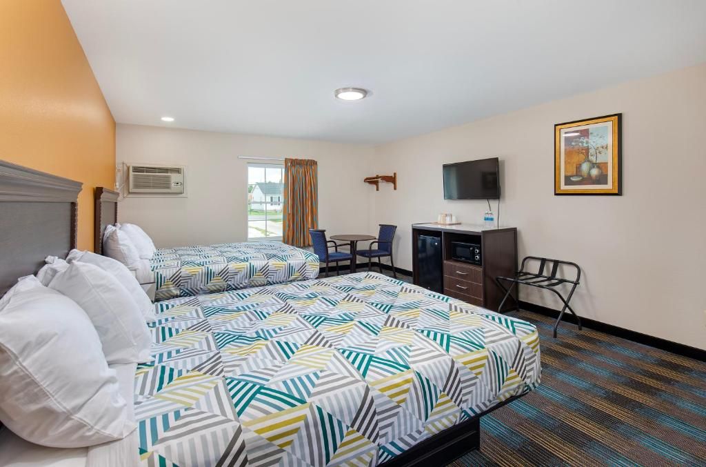 A hotel room with two beds, a desk, a chair, a television, and a window with curtains.