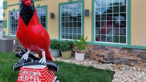 A large red bird sculpture in front of a motel with green trim and multiple windows. - Cardinal Motel (Bowling Green)