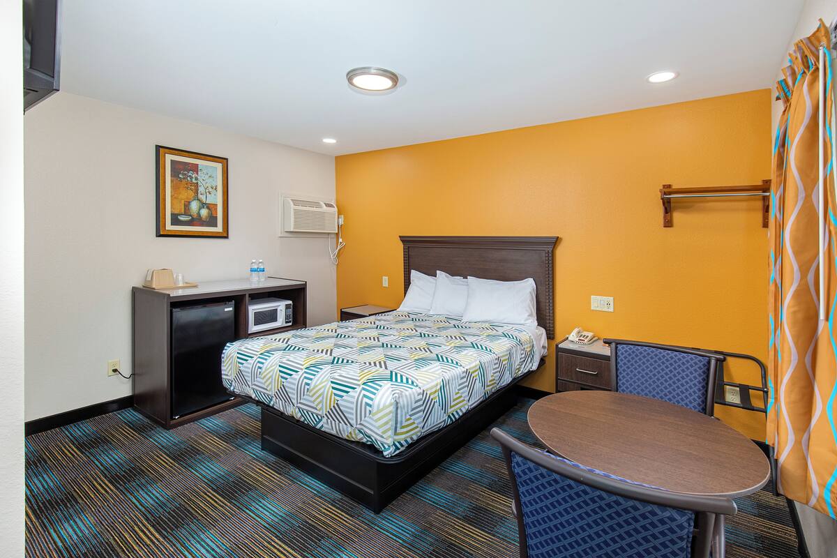 Quarto de hotel com cama, mesa de cabeceira, escrivaninha e uma pequena mesa redonda.