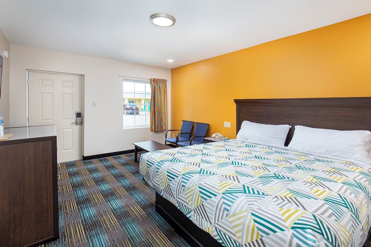 Quarto de hotel com cama, escrivaninha, cadeira e janela com cortinas.