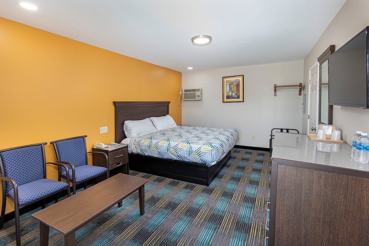 Quarto de hotel com cama, duas cadeiras, escrivaninha e espelho no banheiro.