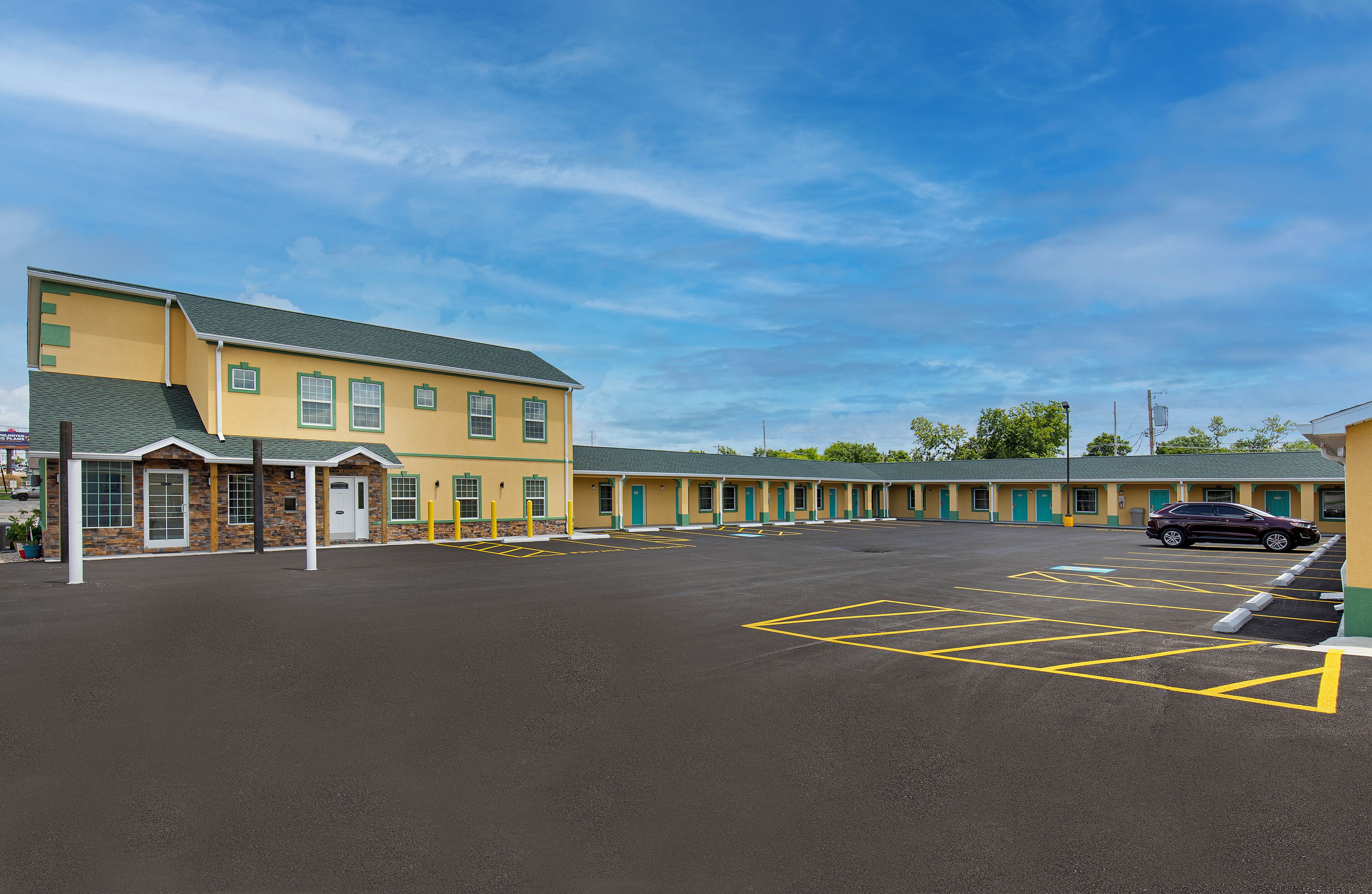 A motel with a large parking lot and a row of rooms with green doors.