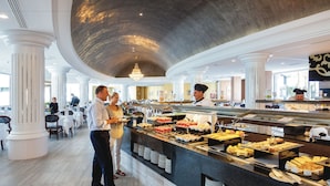A buffet area with a variety of food options, a chef, and a couple standing by the counter. - Hotel Riu Palace Tenerife (Adeje)