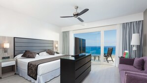 A modern hotel room with a bed, a desk, a chair, and a view of the ocean. - Hotel Riu Palace Tenerife (Adeje)