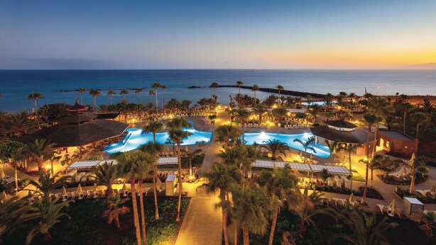 An aerial view of a resort with multiple swimming pools, palm trees, and beachfront access. - Hotel Riu Palace Tenerife (Adeje)