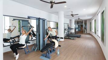 Un gimnasio con equipamiento de ejercicio, ventanas amplias y ventiladores de techo.