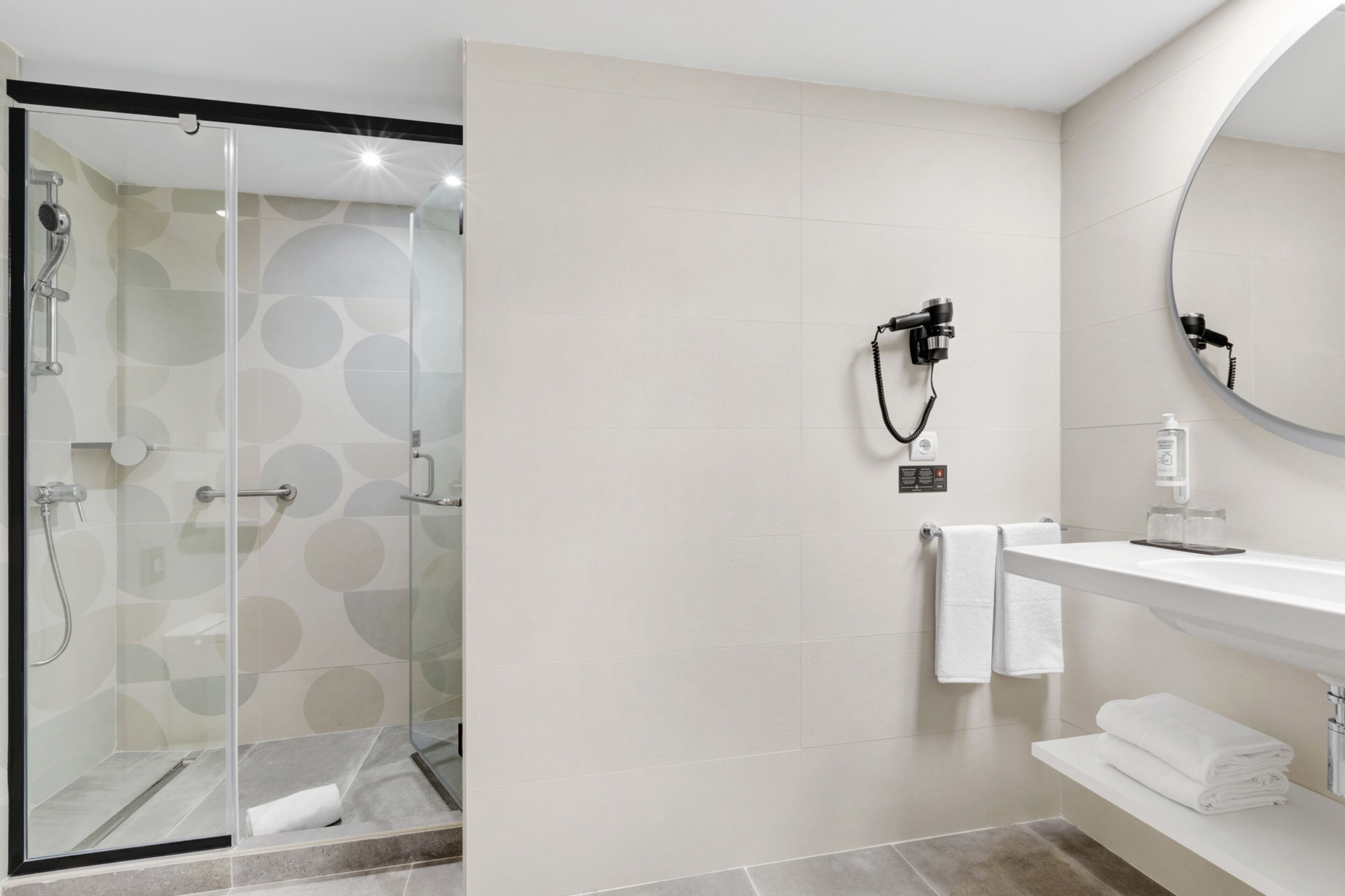 A modern bathroom with a glass-enclosed shower, a white vanity with a mirror, and a towel rack.