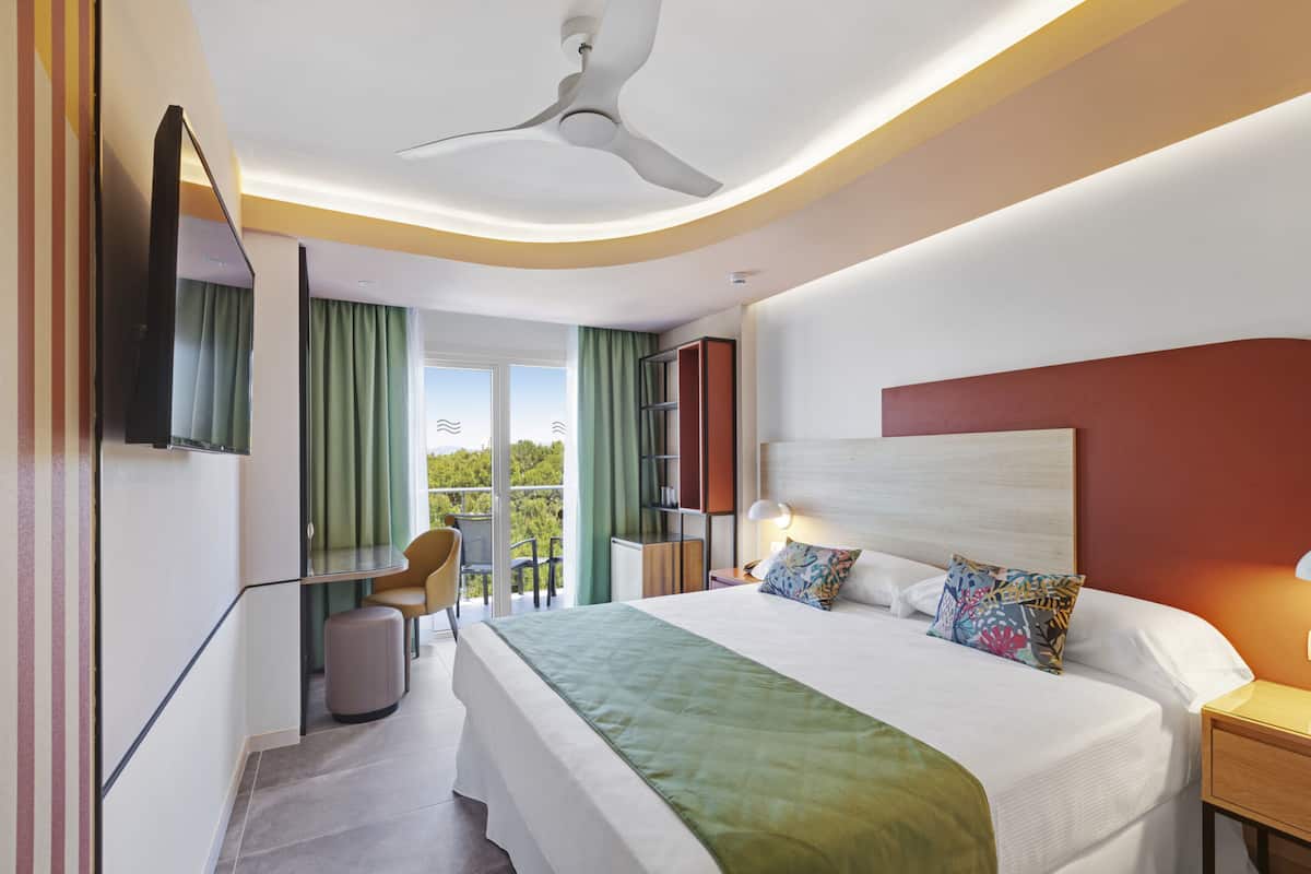 Quarto de hotel moderno com uma cama grande, uma escrivaninha e uma cadeira. Há uma varanda com vista para o exterior.