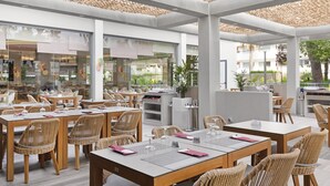 Un área de comedor al aire libre con sillas y mesas de mimbre, separadores de vidrio y un techo con diseño texturizado.