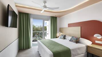 Una habitación de hotel con cama, mesita de noche, televisor y balcón con cortinas.