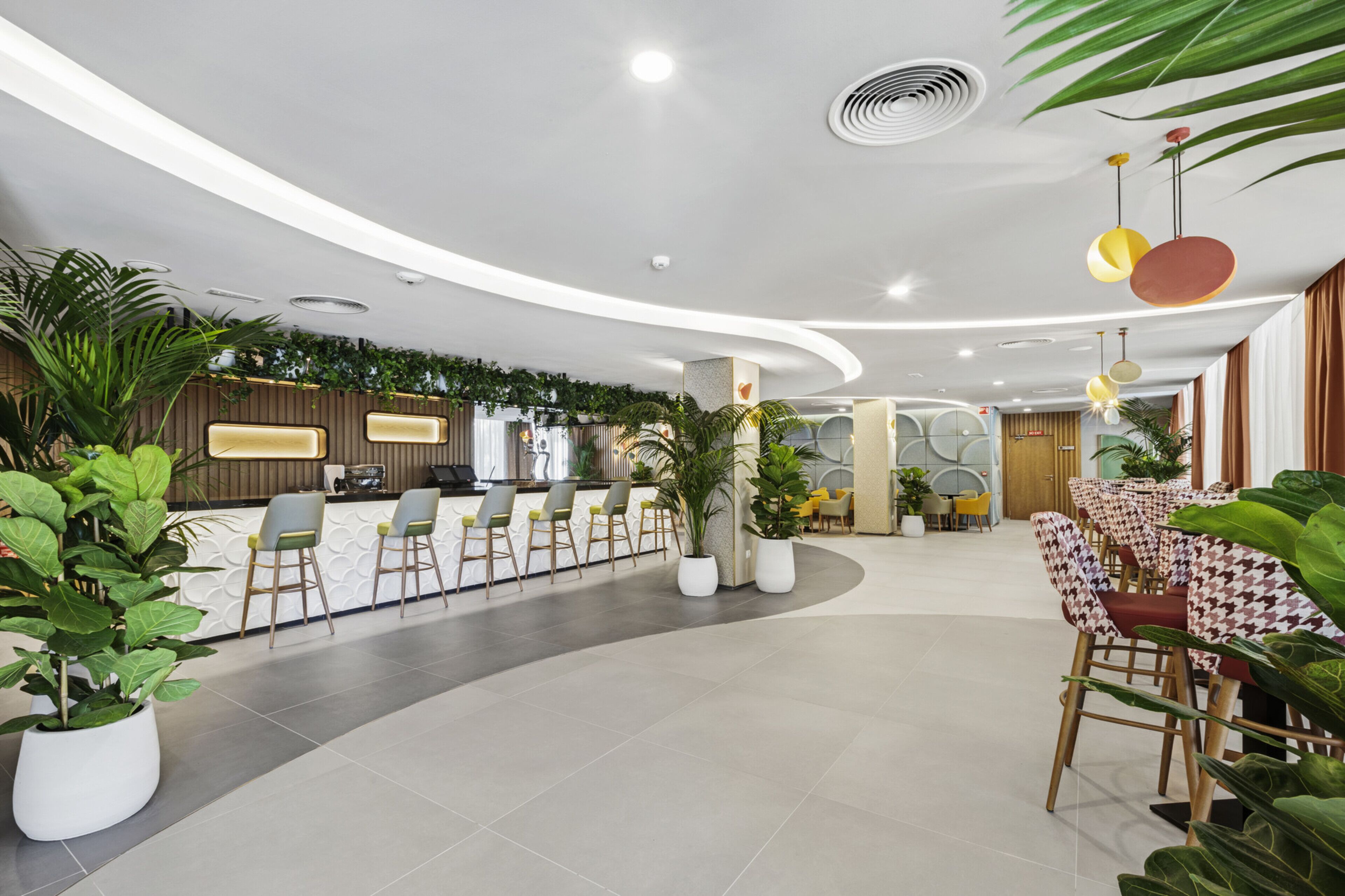 A modern hotel lobby with a reception desk, seating area, and potted plants.