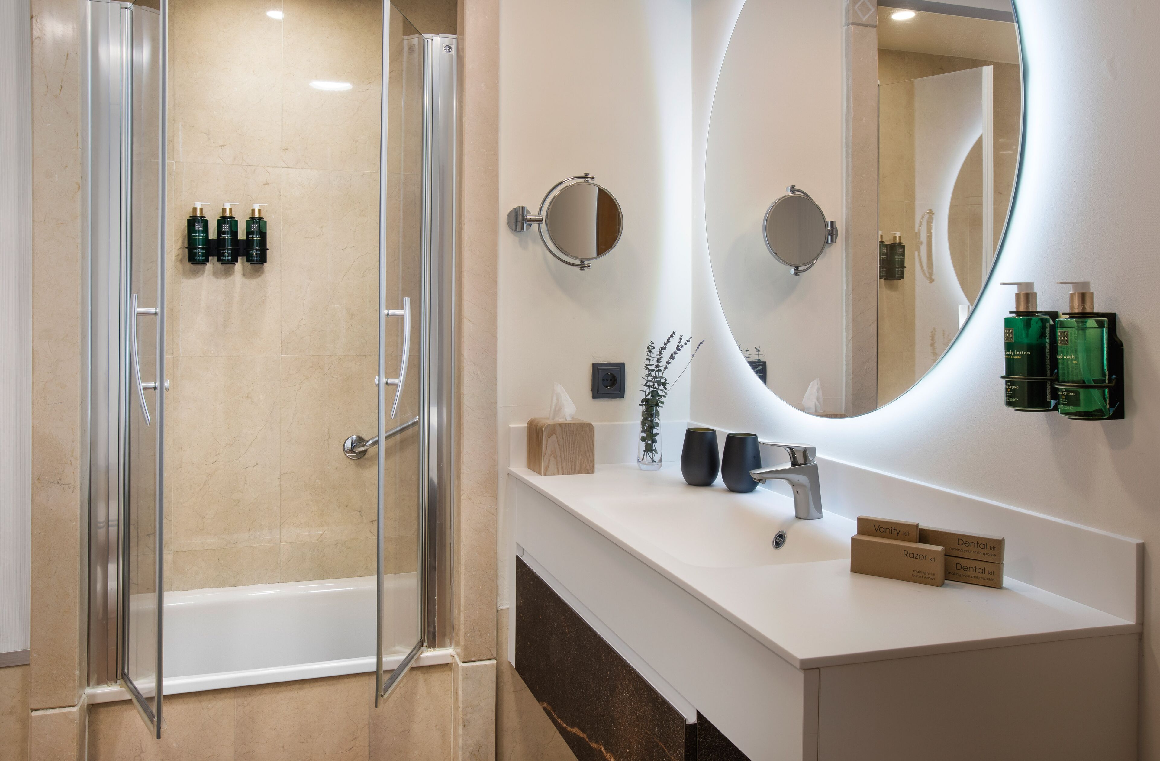 Un baño moderno con cabina de ducha de vidrio, un espejo grande y un tocador blanco con artículos de aseo.