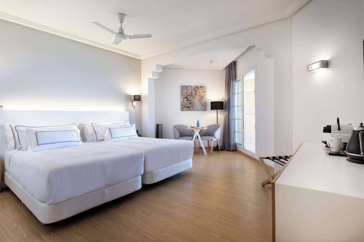 Une chambre d’hôtel avec deux lits, un ventilateur de plafond, un bureau avec une machine à café et une télévision.