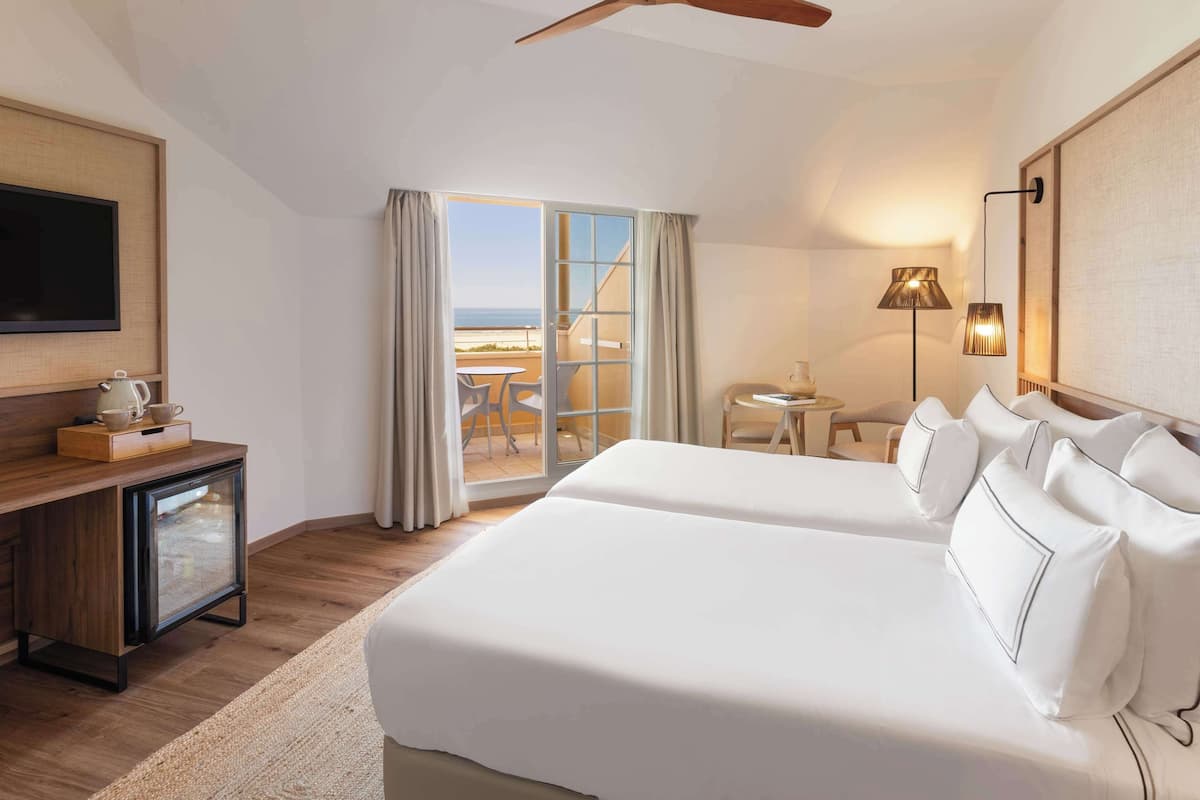 Une chambre d’hôtel dotée d’un grand lit, d’une télévision, d’un coin café et offrant une vue sur la mer grâce à une porte coulissante.