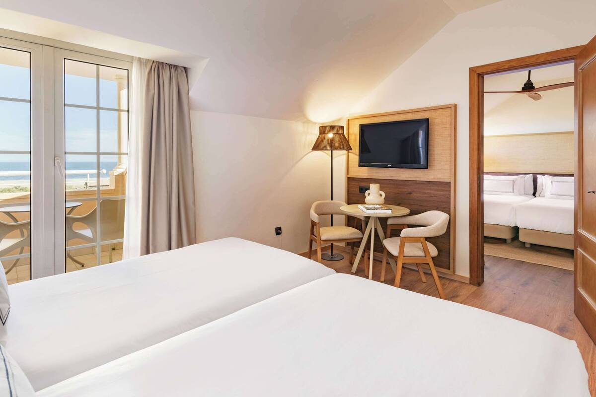 Une chambre d’hôtel avec deux lits, une télévision, une table avec des chaises et une vue sur l’océan.