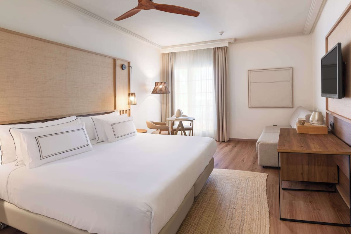 Une chambre d’hôtel avec un grand lit, un bureau, une chaise, une lampe et un téléviseur.