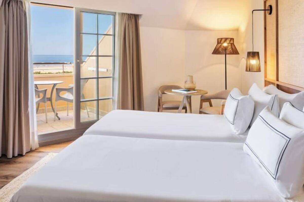 Une chambre d’hôtel avec un grand lit, une petite table, une chaise et une vue sur la plage.